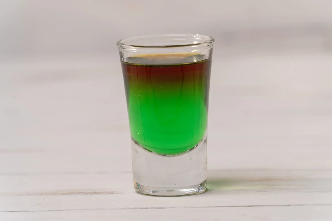 After Six Shot: Vibrant layered cocktail shot glass with a gradient from green to brown on a white background.