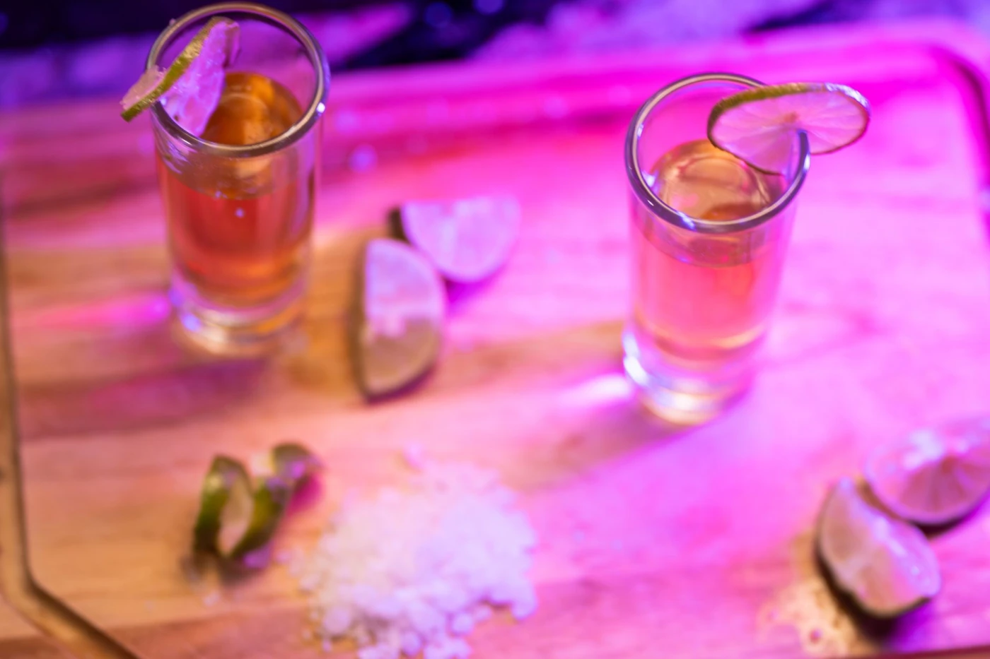 Batanga Tequila and Coke Cocktail: A shot of tequila garnished with lime, surrounded by lemon slices and salt on a wooden board.