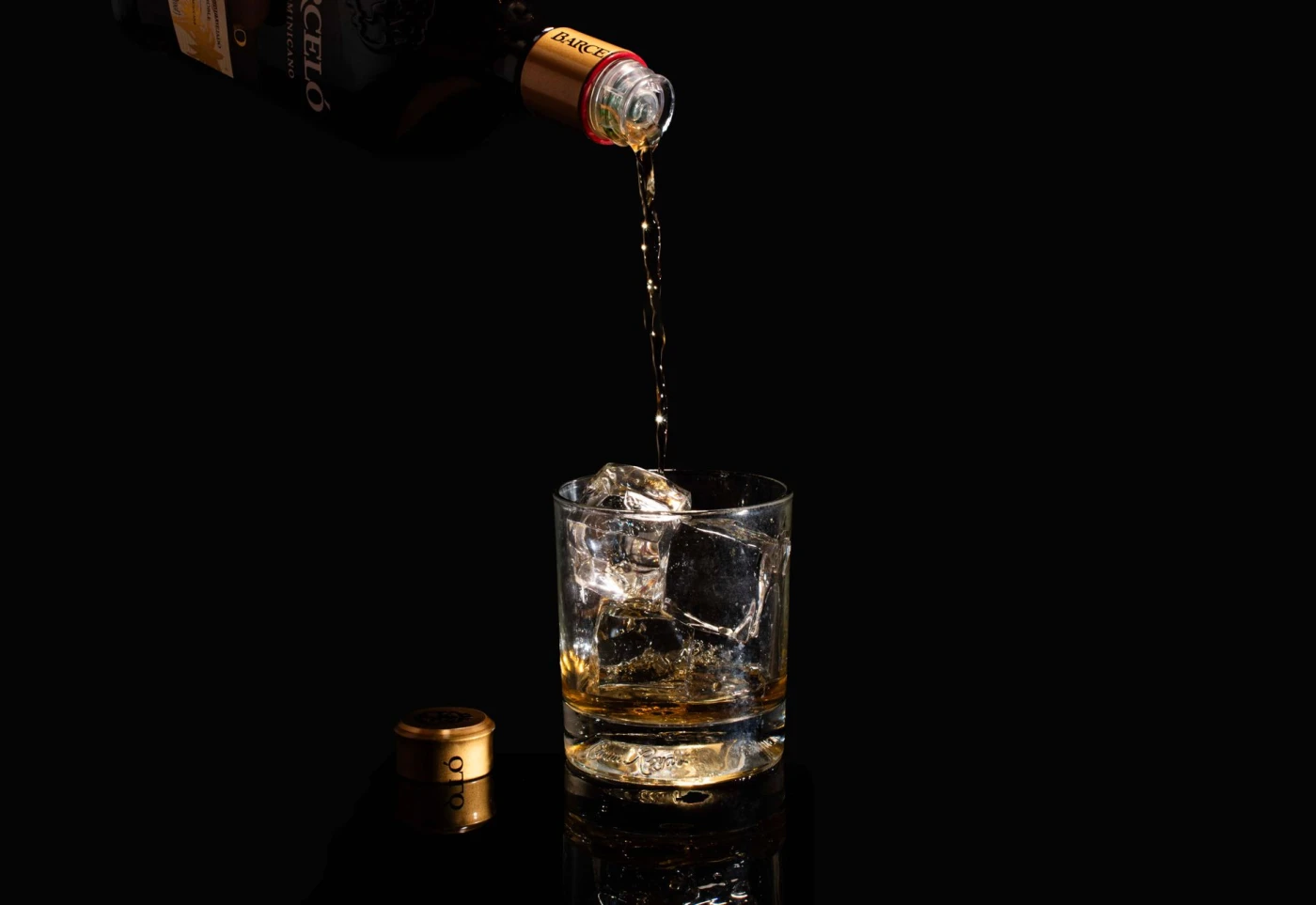 Blacktail’s Rum and Coke: Golden rum being poured into a glass filled with ice on a black background.