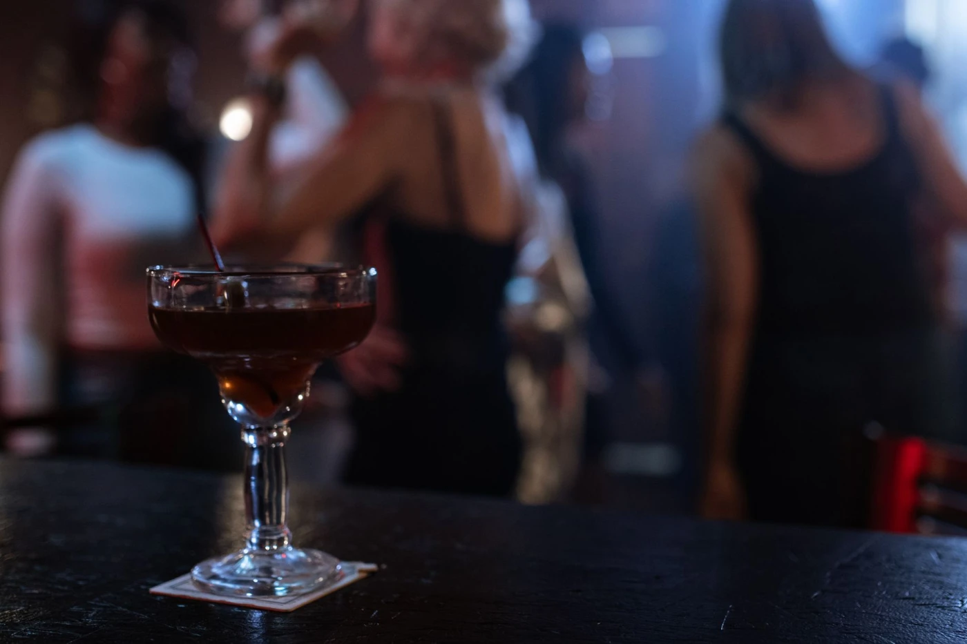 Clover Club: A lively nightclub atmosphere with focus on a cocktail and blurred party background.