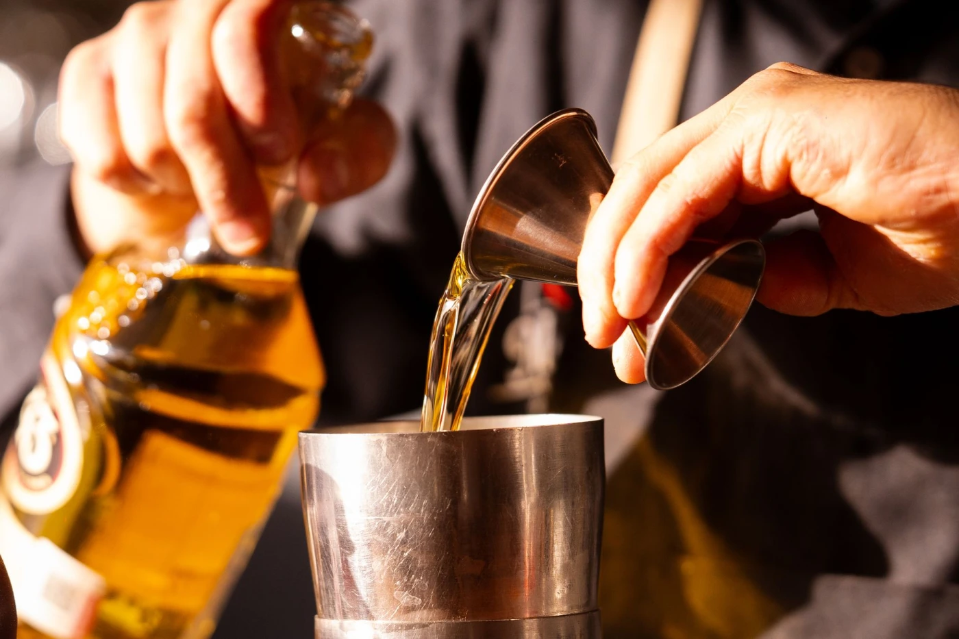 Cornish Gold Rum Old Fashioned: Close-up of a bartender pouring a golden beverage into a cocktail shaker with careful precision.