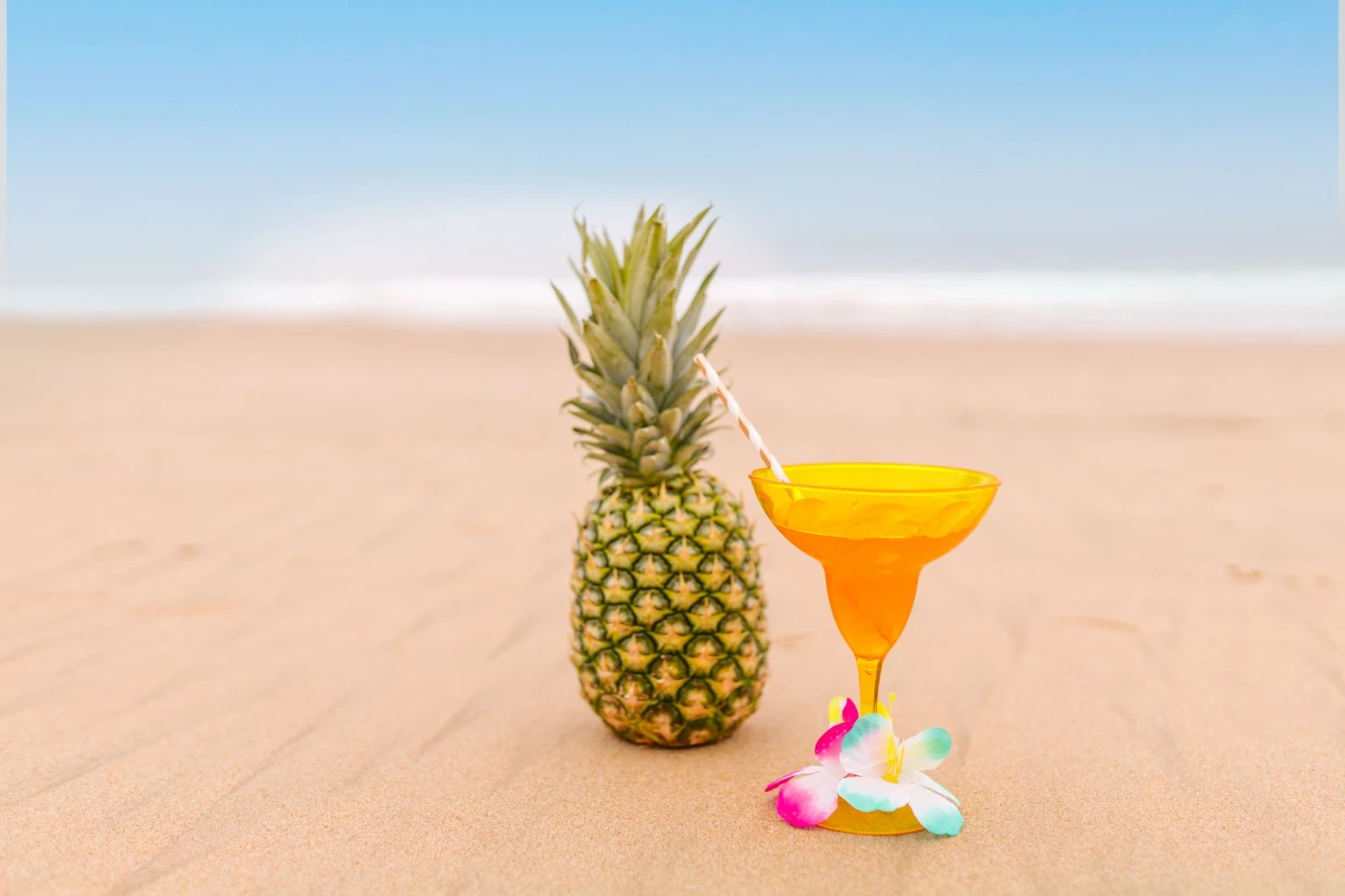 Vibrant pineapple and spiced rum cocktail with a straw on a sandy beach