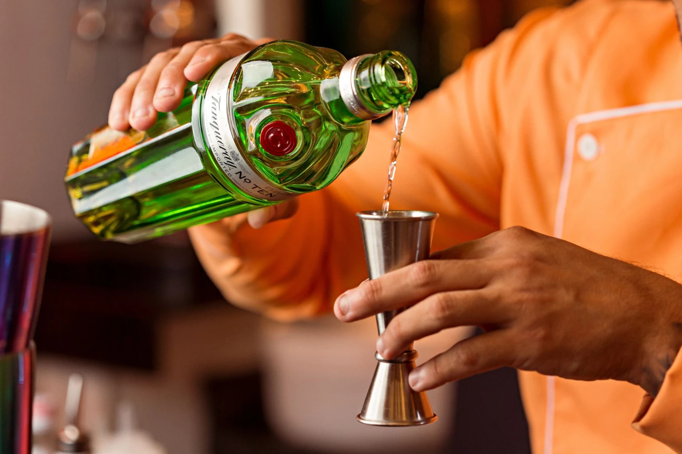How Gin Is Made: Close-up of a bartender pouring gin into a jigger, preparing a cocktail.
