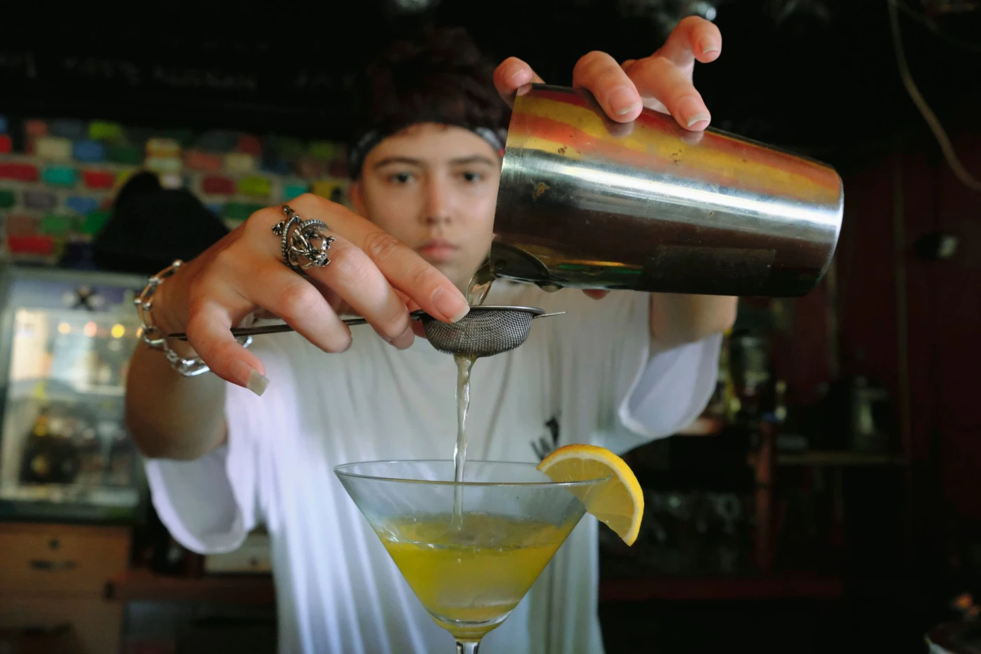 A bartender skillfully pouring a citrus cocktail through a strainer, enhancing the drink's flavor in a dimly lit bar.