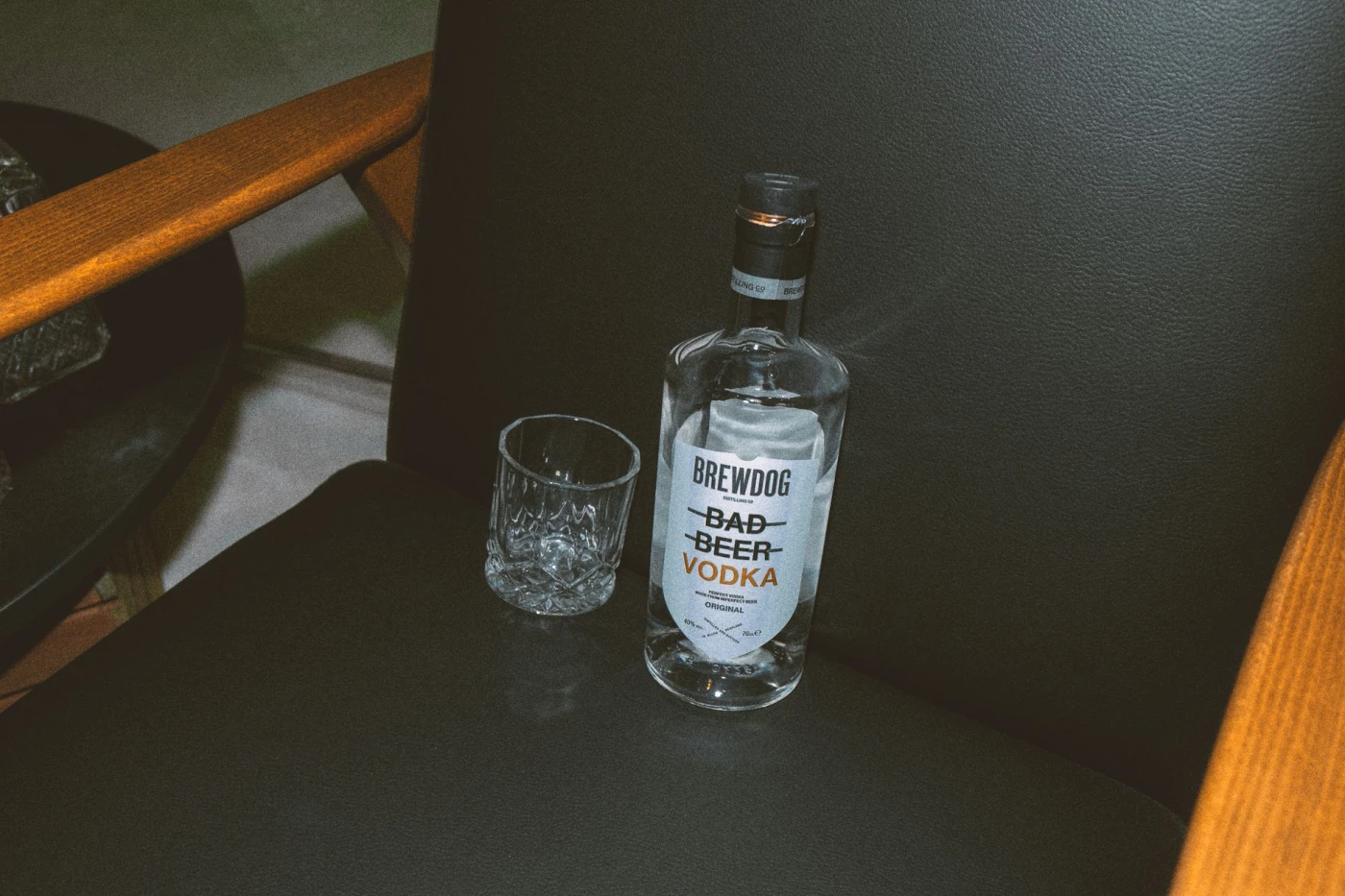 Vodka bottle and glass on a sleek black chair, showcasing refined elegance in dim lighting.