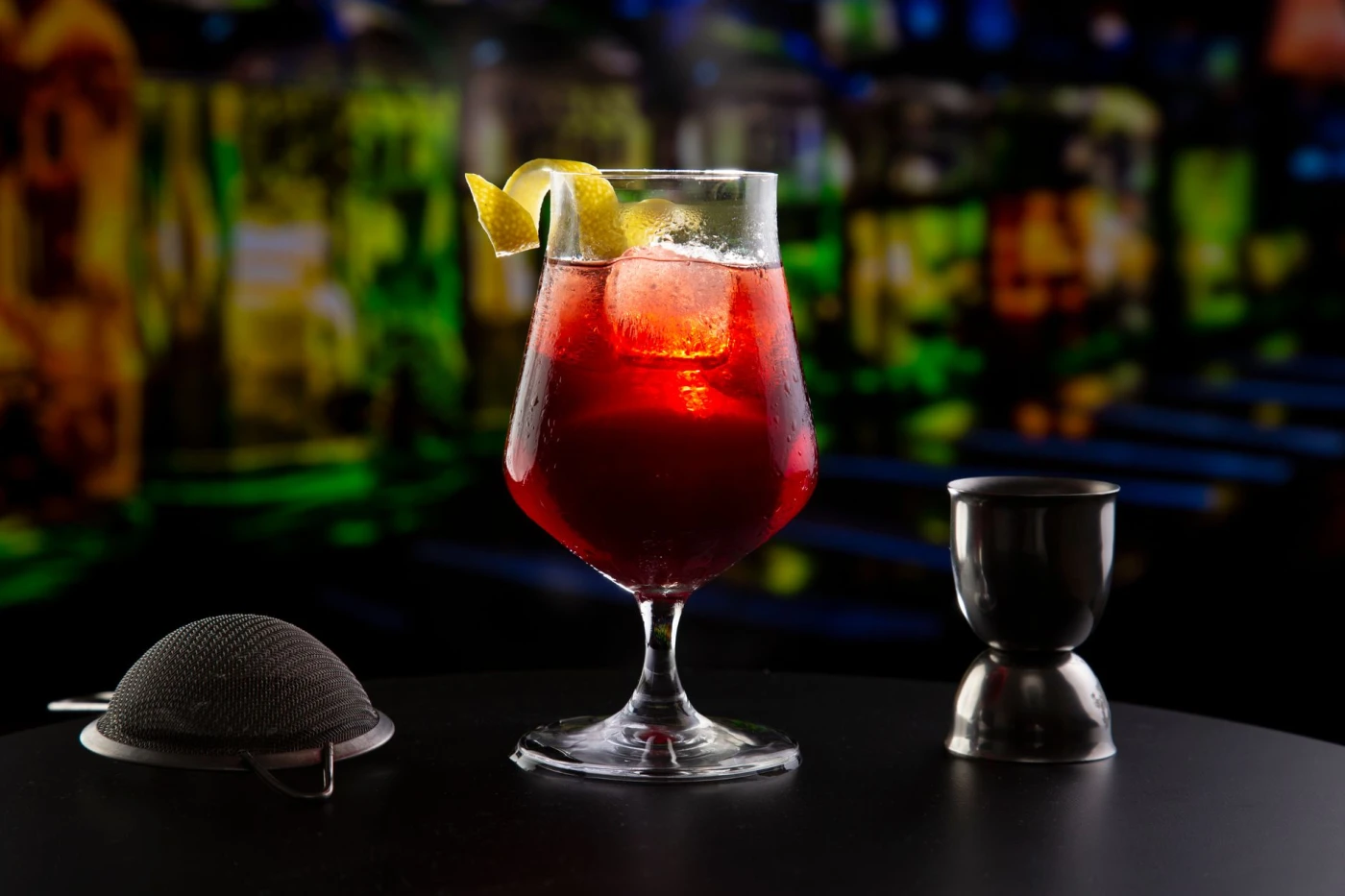 A colorful cocktail with ice and citrus garnish, set against moody bar lighting, perfect for nightlife and drink themes.