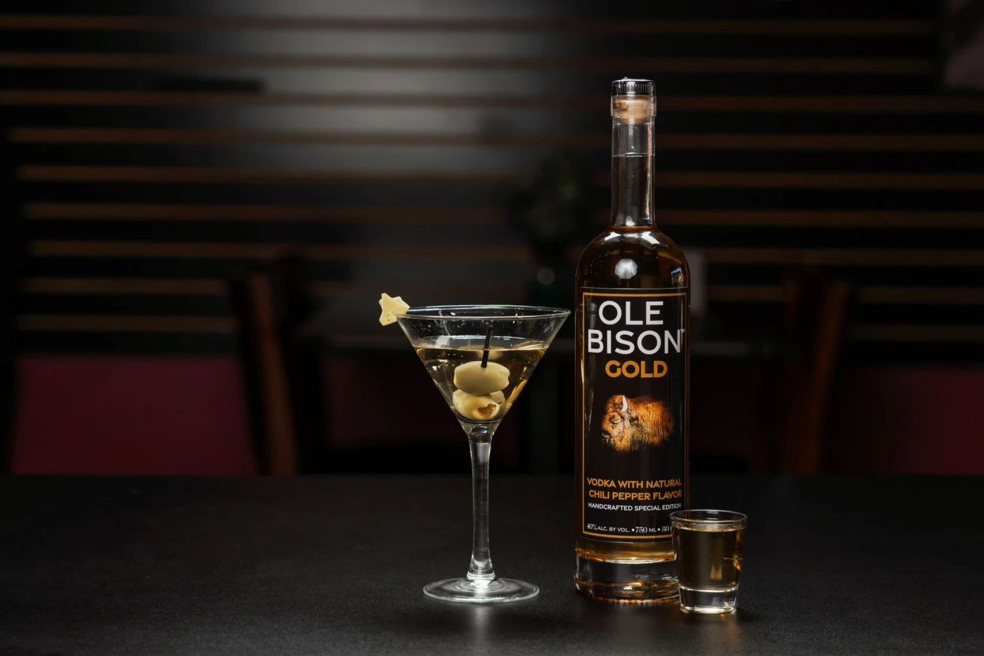Sophisticated bar presentation with Ole Bison Gold Vodka, martini glass, and shot glass on a dark countertop.