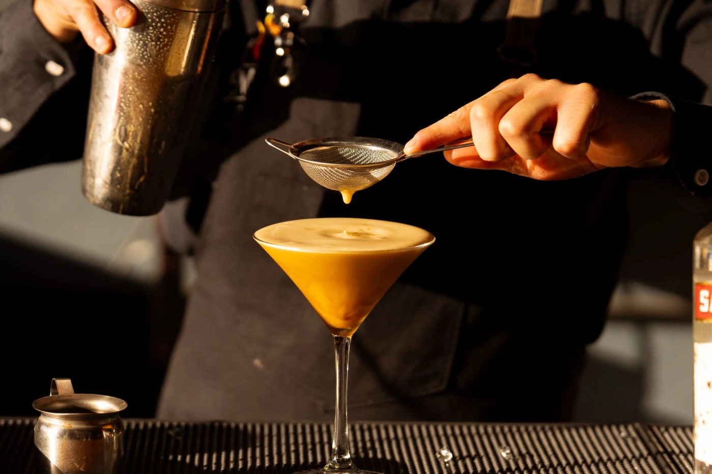 Close-up of a bartender pouring a cocktail through a strainer in a stylish café setting.
