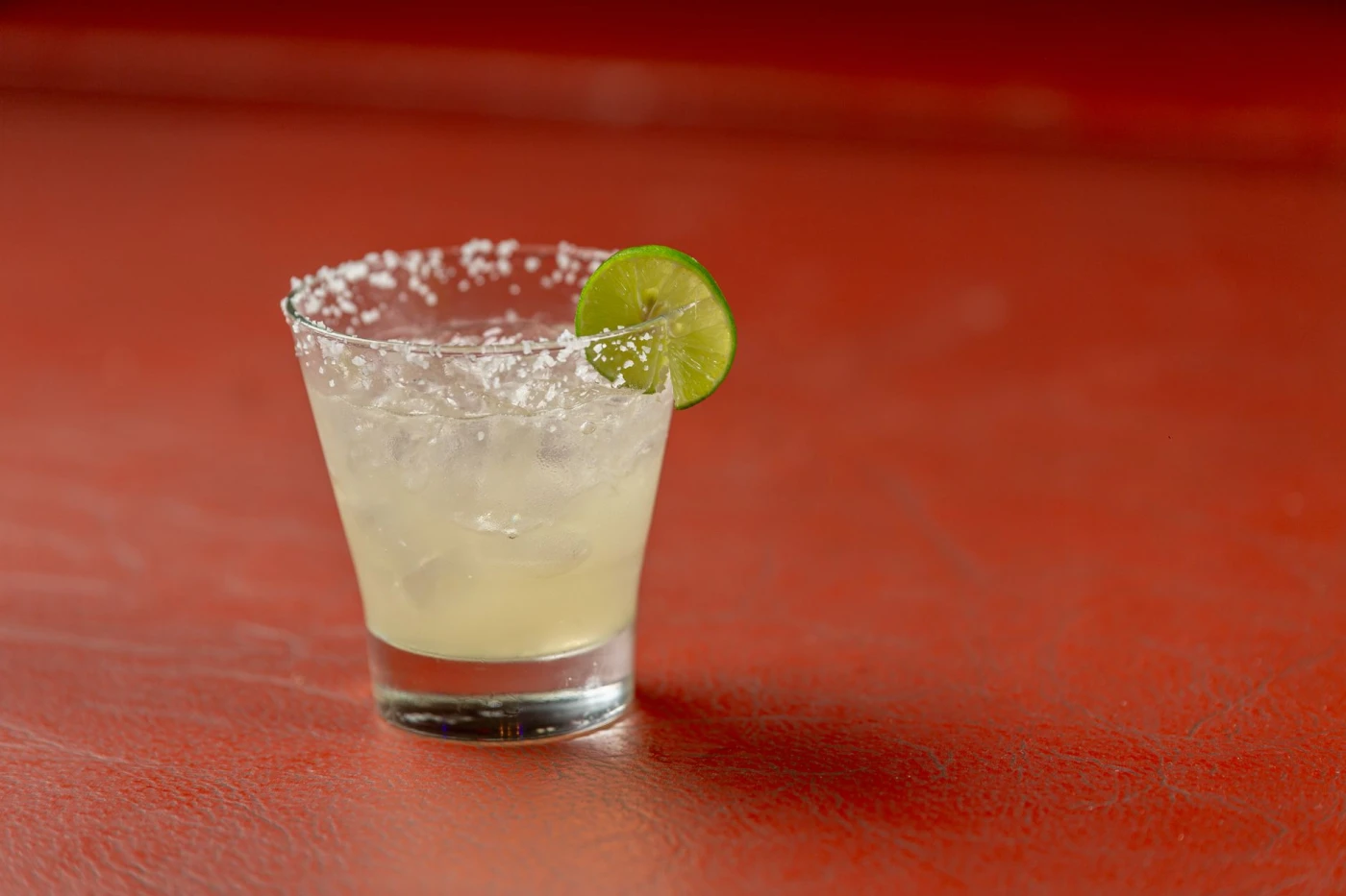 Phil Ward’s Margarita: A classic margarita cocktail with lime, salt rim, on a textured red background, perfect for cocktail