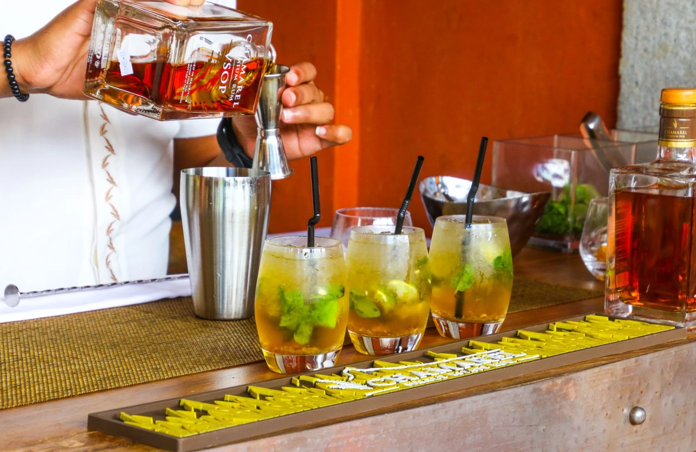 Spring Rum Serves to Brighten Your Days: Bartender pouring rum into cocktail glasses at a vibrant bar setting.