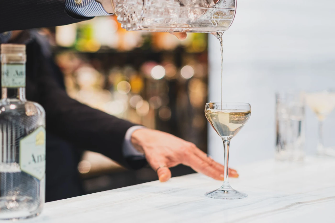 The History of Gin: Britain’s Own Spirit, Born of Chaos and Craft: Close-up of bartender pouring gin into a glass for a martini, showcasing cocktail preparation at a P