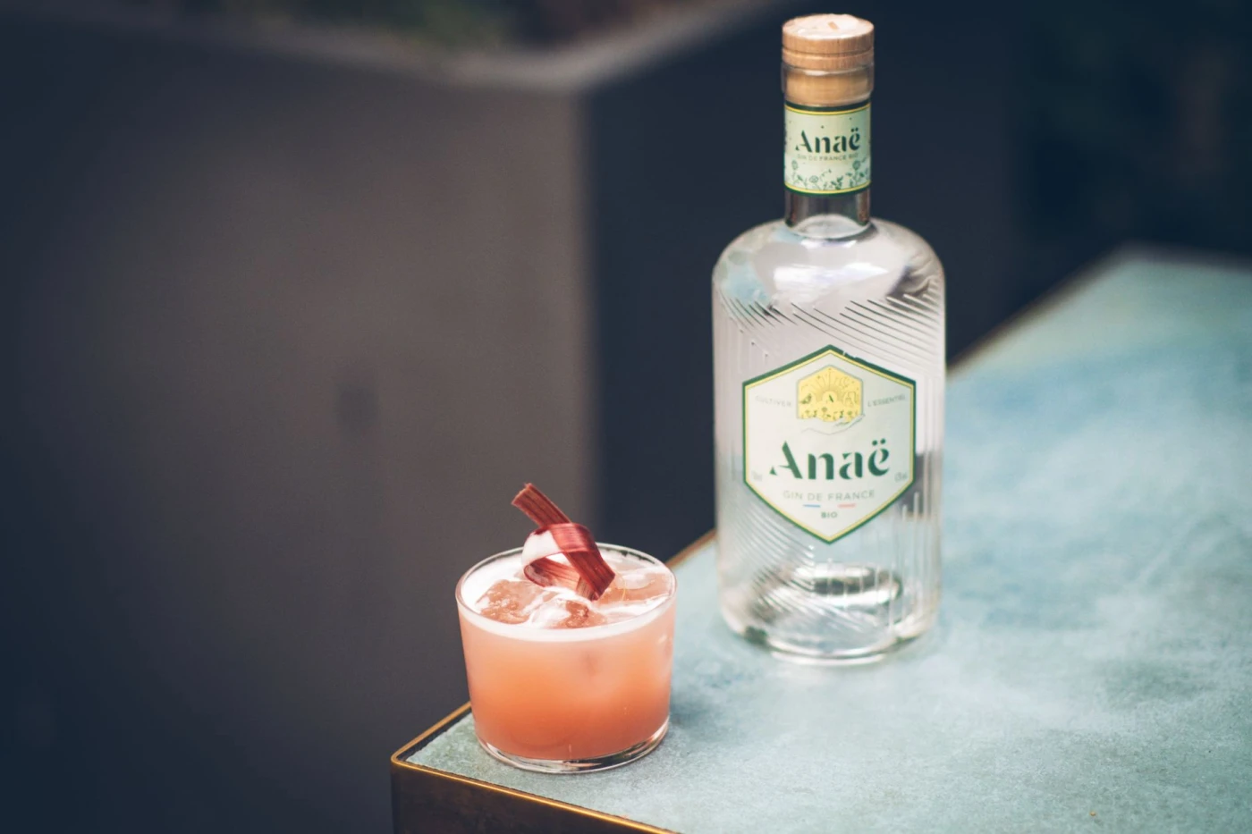 Refreshing pink craft gin cocktail next to a bottle of Anae gin on a sleek table