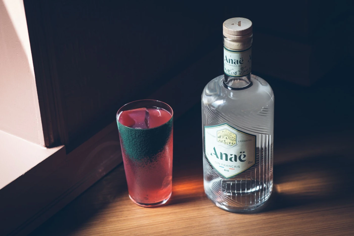 Stylish presentation of Anae gin bottle beside a refreshing cocktail glass on a wooden surface