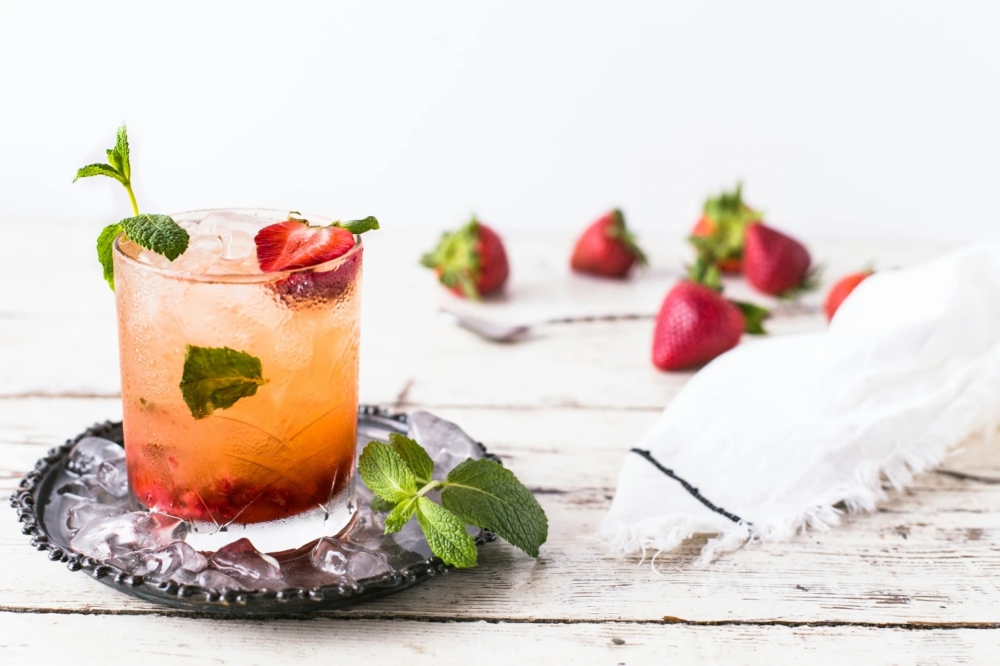 Whiskey Smash cocktail with muddled strawberries, fresh mint, and crushed ice in a rocks glass